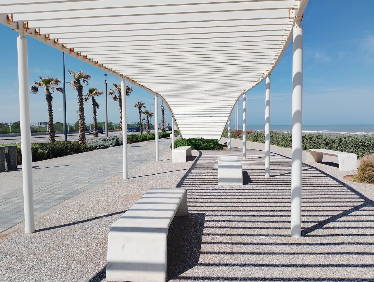 White pergola casting geometric shadows by the beach with palm trees in Casablanca.